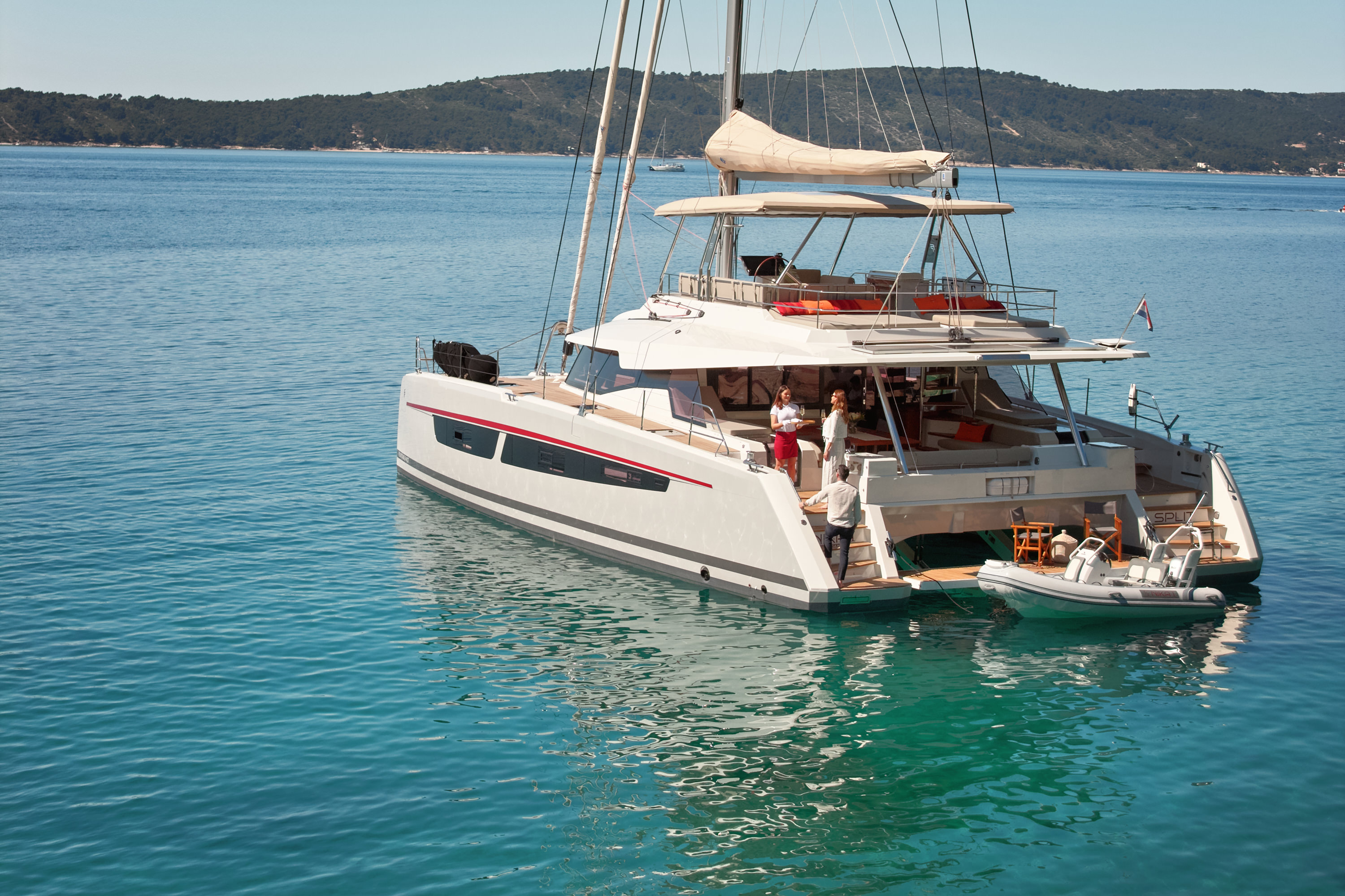 Aerial diagonal overhead, full catamaran hull visible, clear blue water, strong composition