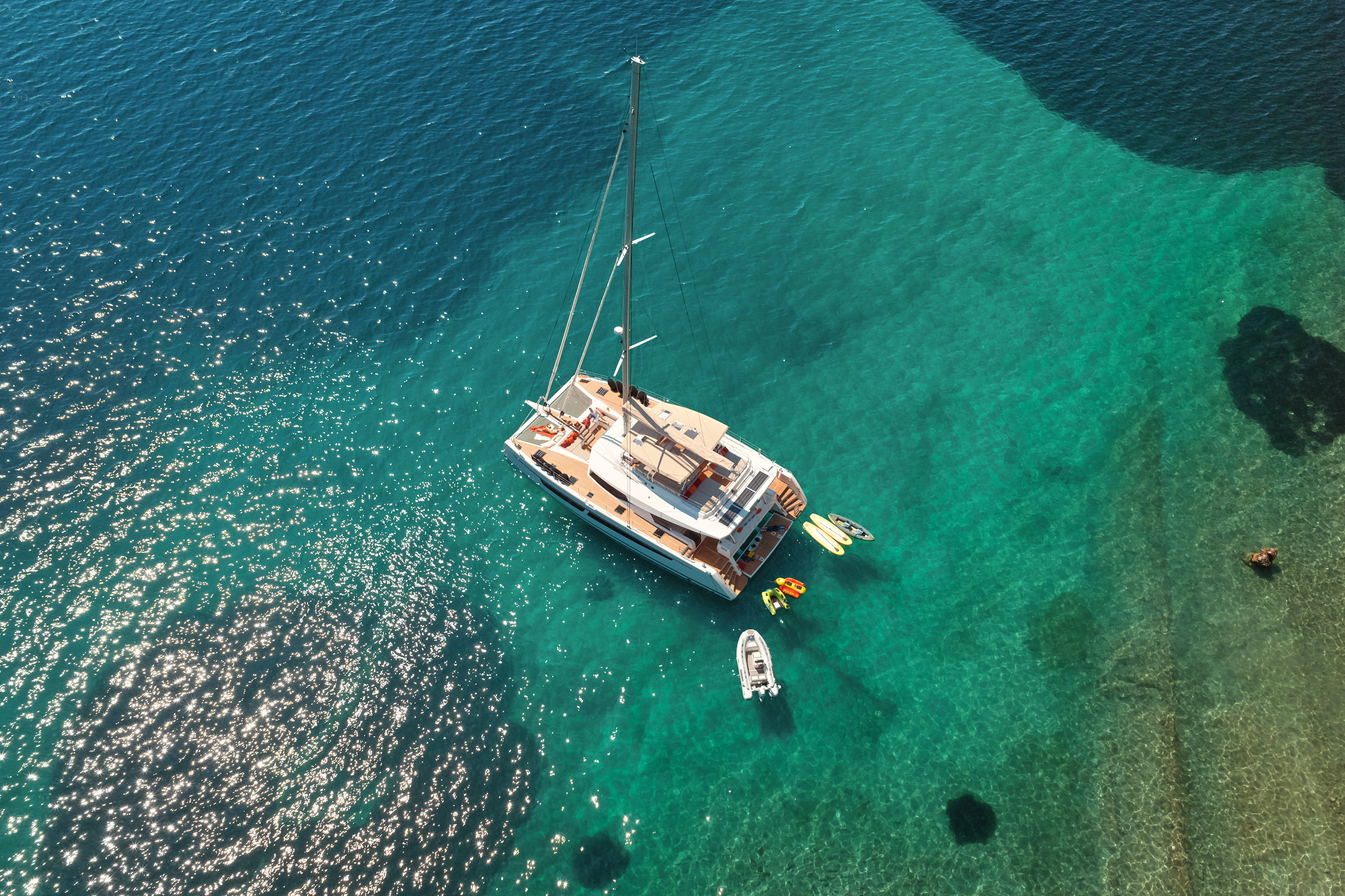 Aerial top-down, NIKA I at anchor with water toys deployed, crystal clear turquoise water, sea floor