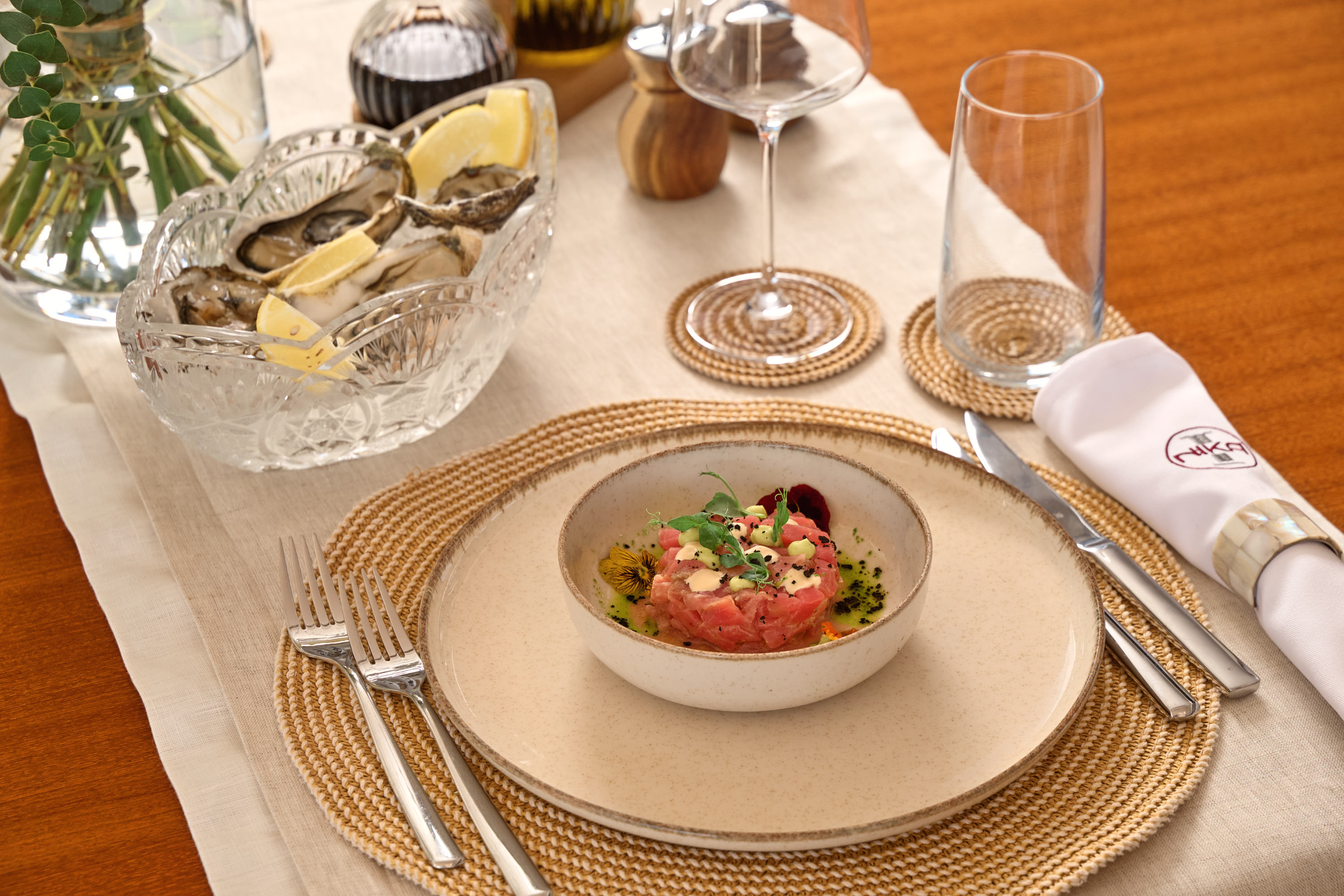 Tuna tartare with fresh oysters, crystal glassware, NIKA napkin ring, fine dining plating on teak table
