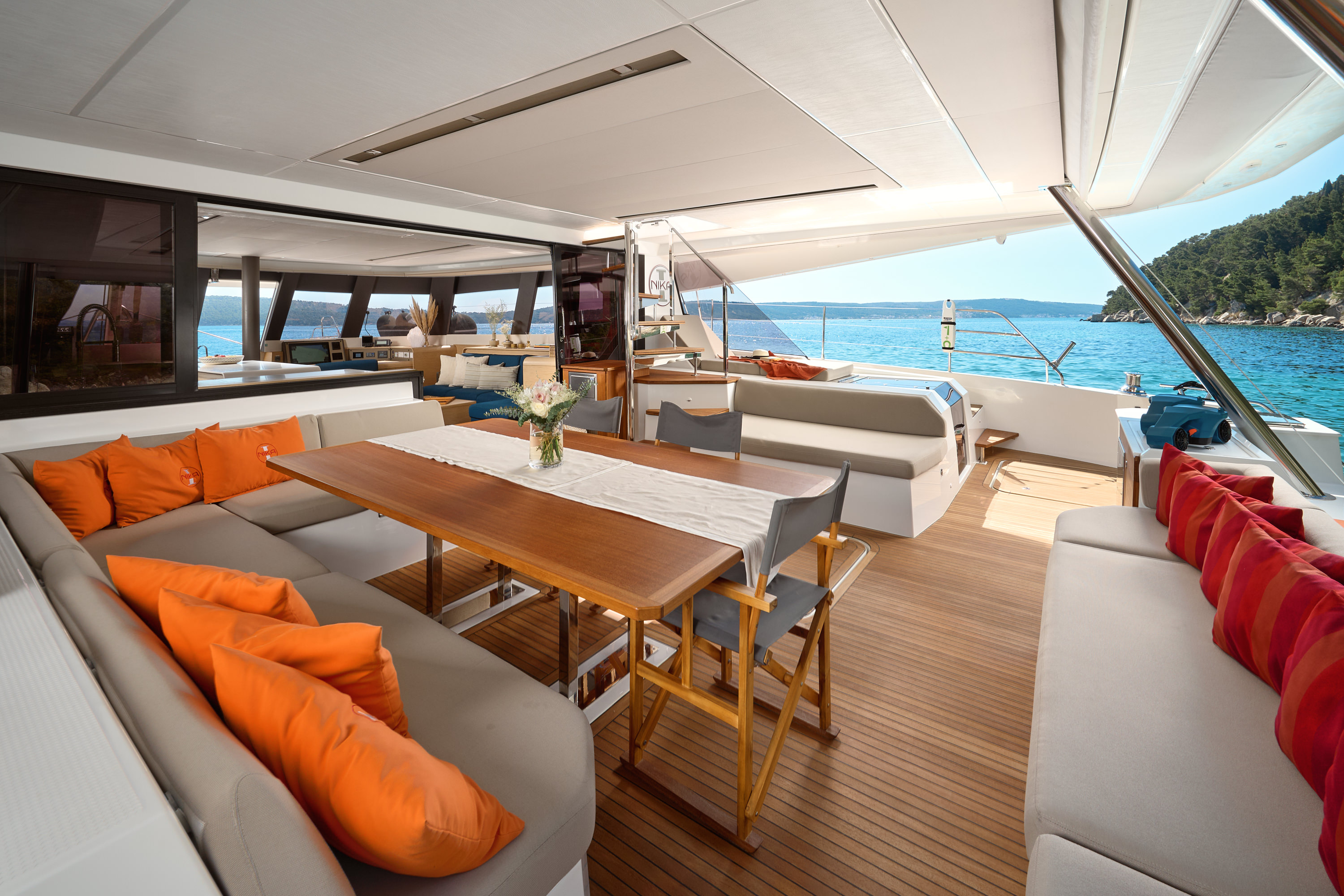 Couple relaxing on foredeck sunbeds under sail, open Adriatic, orange cushions, sunny day at sea