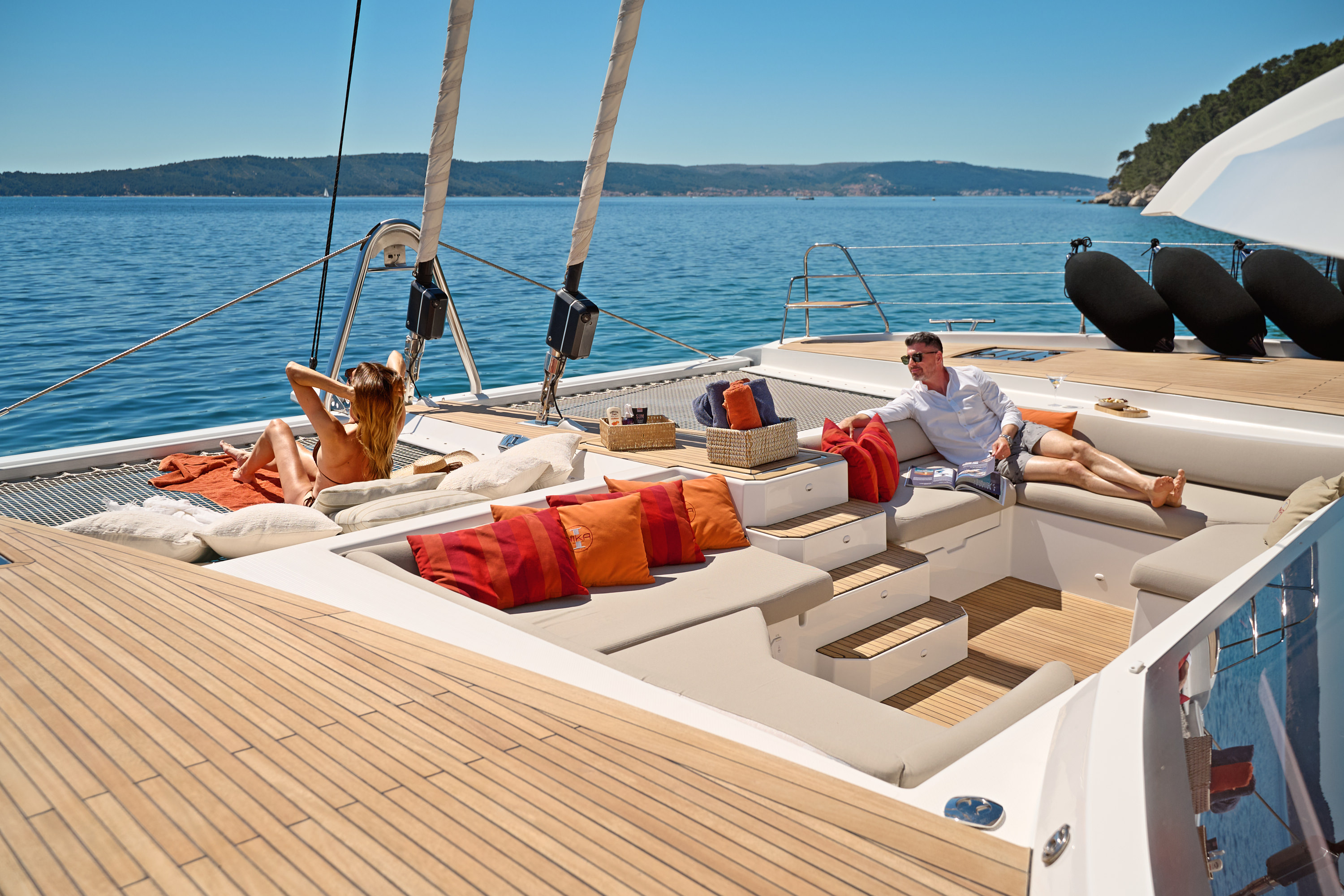 Aft cockpit dining area, teak table set, open transom doors to sea and island, orange cushions, Adriatic