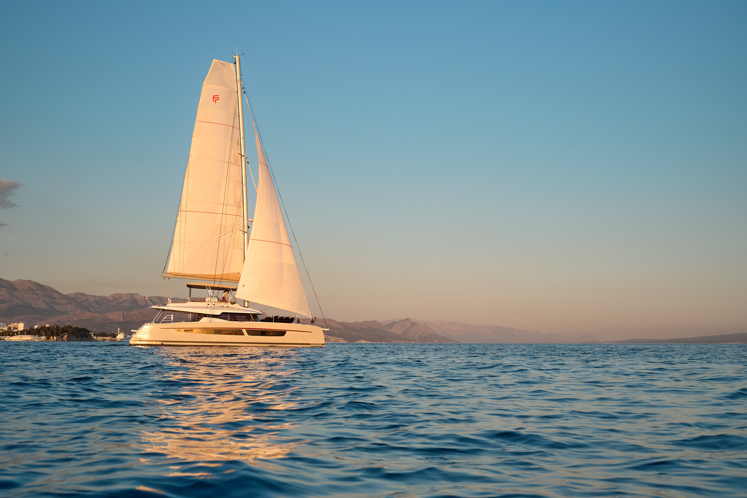 Sailing at sunset, warm golden tones, mountain silhouette, full sail, magazine cover quality